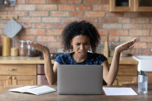 Confused woman gesturing incredulously in response to something on her laptop screen